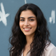 Portrait of a smiling Emirati woman with long, slightly frizzy dark hair, looking confidently at the camera.